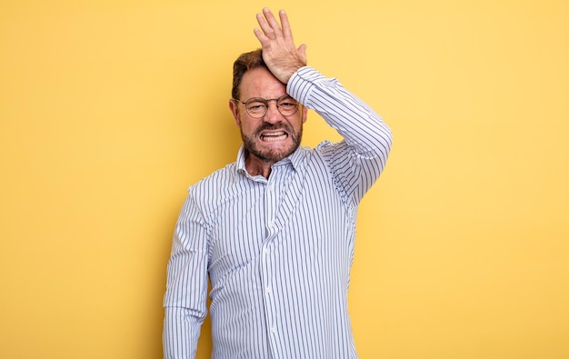 Homem bonito de meia-idade erguendo a palma da mão na testa pensando opa, depois de cometer um erro estúpido ou lembrar, sentindo-se idiota