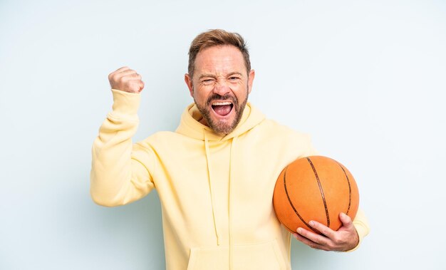 Homem bonito de meia-idade gritando agressivamente com um conceito de basquete de expressão de raiva