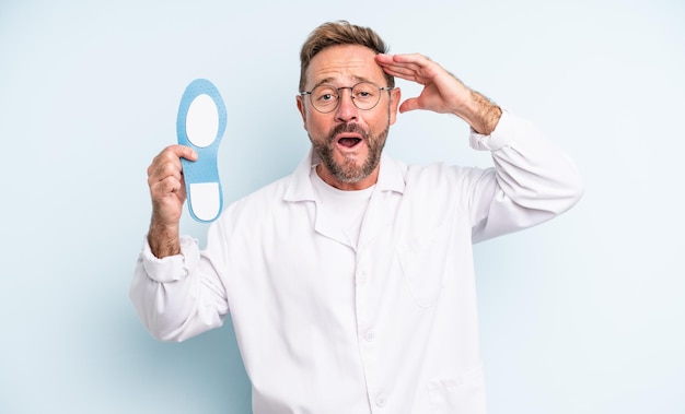 Homem bonito de meia-idade olhando feliz conceito de podólogo surpreso e surpreso