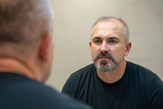 Homem bonito de meia idade olhando no espelho no banheiro depois de fazer a barba