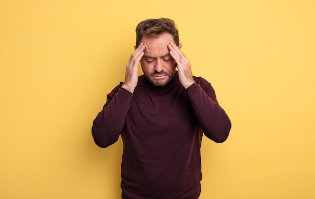 Homem bonito de meia-idade parecendo estressado e frustrado, trabalhando sob pressão, com dor de cabeça e preocupado com problemas