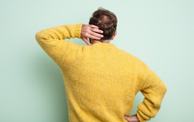 Homem bonito de meia-idade pensando ou duvidando, coçando a cabeça, sentindo-se confuso e confuso, vista traseira ou traseira