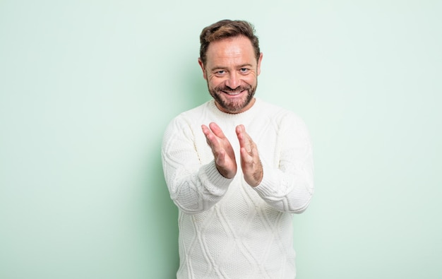 Homem bonito de meia-idade se sentindo feliz e bem sucedido, sorrindo e batendo palmas, dizendo parabéns com aplausos