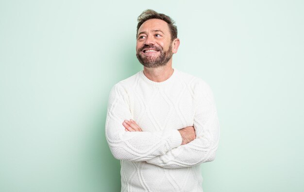 Homem bonito de meia-idade se sentindo feliz, orgulhoso e esperançoso, imaginando ou pensando, olhando para cima para copiar o espaço com os braços cruzados