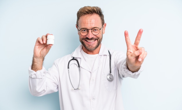 Homem bonito de meia-idade sorrindo e parecendo feliz, gesticulando vitória ou paz. médico com frasco de comprimidos