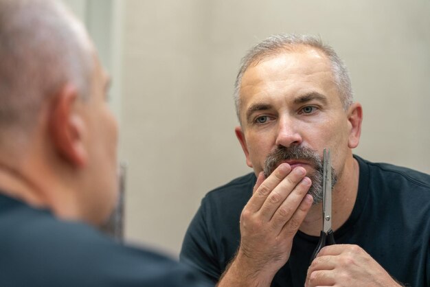 Homem bonito de meia-idade usando tesoura para cortar a barba um pouco e corrigir a forma