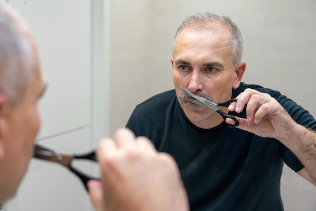 Homem bonito de meia idade usando tesoura para cortar o bigode