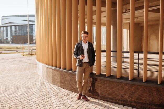 Homem bonito de óculos com um smartphone na rua de uma cidade grande. Empresário falando ao telefone em meio urbano