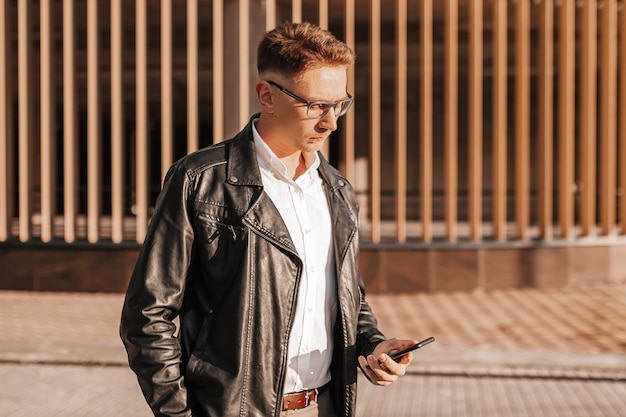 Homem bonito de óculos com um smartphone na rua de uma cidade grande. empresário falando ao telefone em meio urbano