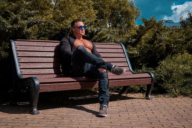 homem bonito de óculos, vestindo uma camisa preta e jeans, sentado em um banco no parque