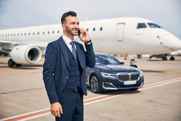 Homem bonito de terno falando ao telefone em frente a um avião