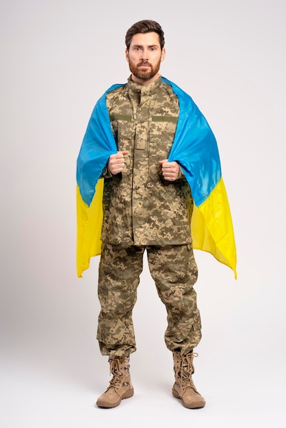 Homem bonito e barbudo, soldado confiante vestindo uniforme de camuflagem militar segurando a bandeira ucraniana