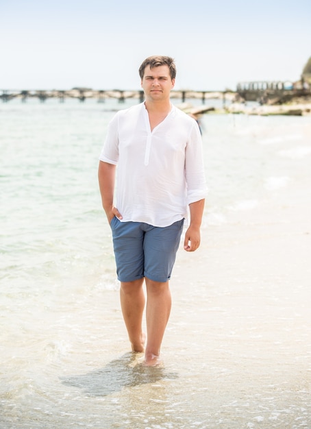 Homem bonito e elegante de camisa branca, caminhando à beira-mar