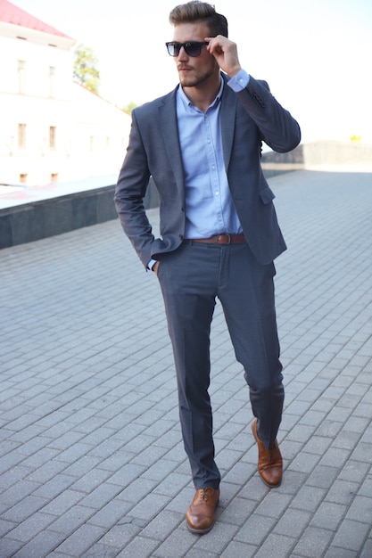 Homem bonito e elegante em um terno elegante e óculos escuros na rua.