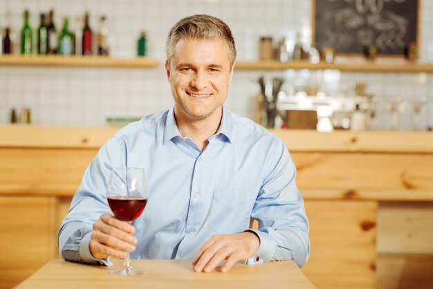 Homem bonito e exuberante, bem construído, bebendo vinho e vestindo uma camisa azul enquanto relaxa