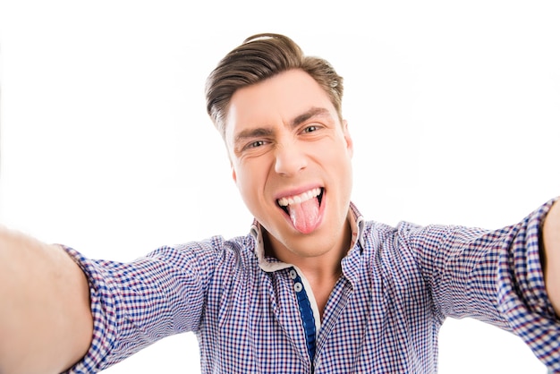 Homem bonito e feliz fazendo selfie cômico e mostrando a língua