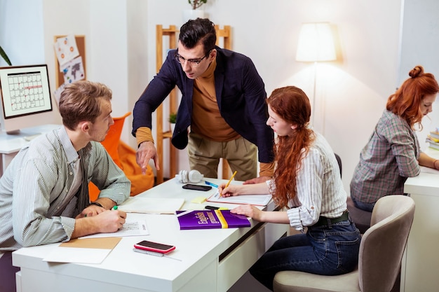 Homem bonito e inteligente apontando com a mão enquanto fala com seu aluno sobre o trabalho de teste