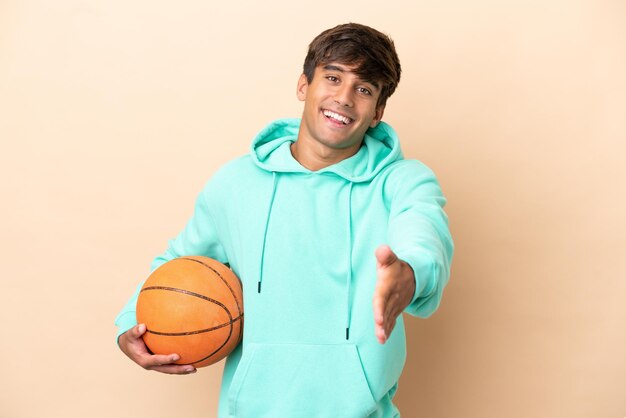 Homem bonito e jovem jogador de basquete isolado em fundo ocre, apertando as mãos para fechar um bom negócio