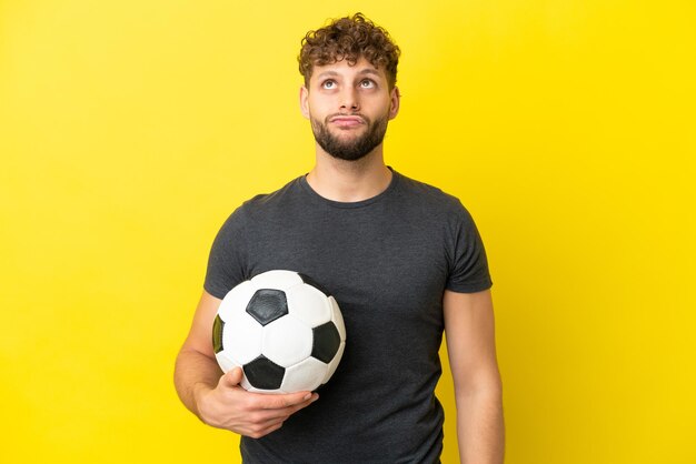 Homem bonito e jovem jogador de futebol isolado em fundo amarelo e olhando para cima