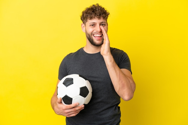 Homem bonito e jovem jogador de futebol isolado em fundo amarelo gritando com a boca aberta