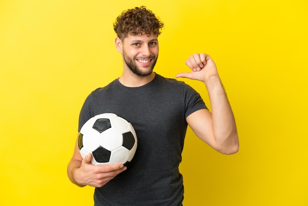 Homem bonito e jovem jogador de futebol isolado em fundo amarelo orgulhoso e satisfeito