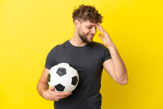 Homem bonito e jovem jogador de futebol isolado no fundo amarelo rindo