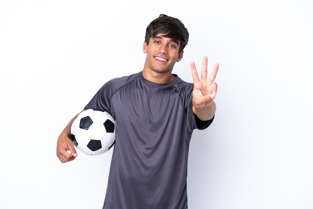 Homem bonito e jovem jogador de futebol isolado no fundo branco feliz e contando três com os dedos