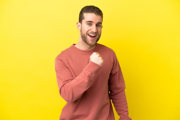 Homem bonito e loiro sobre fundo amarelo isolado comemorando uma vitória