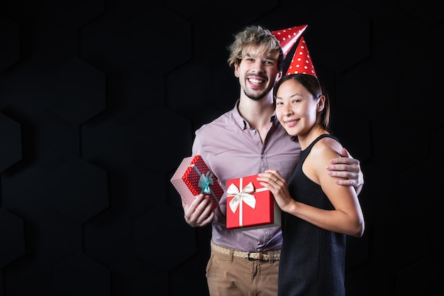 Homem bonito e mulher atraente, olhando para a caixa com presentes em um fundo preto. Conceito de férias.