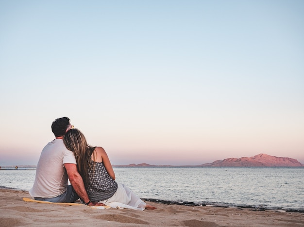 Homem bonito e mulher fofa sentados na praia