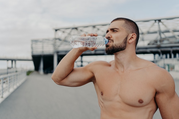 Homem bonito e musculoso com torso nu ao ar livre fazendo exercícios de fitness