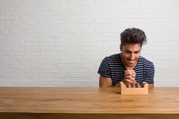 Homem bonito e natural jovem sentado em uma mesa muito feliz e animado, levantando os braços