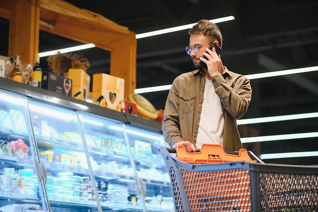 Homem bonito e sorridente a fazer compras no supermercado a empurrar o carrinho