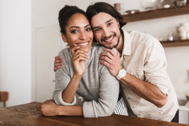 Homem bonito e sorridente abraçando com ar sonhador a linda mulher afro-americana