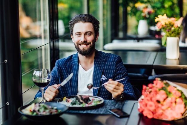 Homem bonito e sorridente comendo salade em restaurante e uma mulher esperando com um buquê de rosas