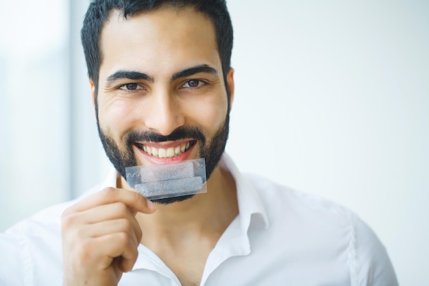 Homem bonito e sorridente segurando uma faixa de clareamento