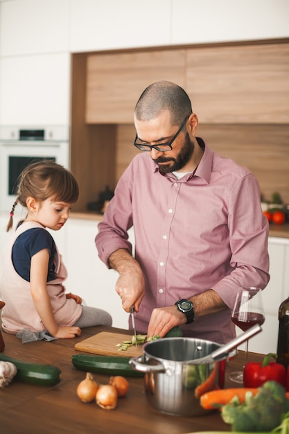Foto homem bonito e sua filha pequena estão cozinhando ensopado de legumes juntos na cozinha. conceito de comida saudável e vegetariana.