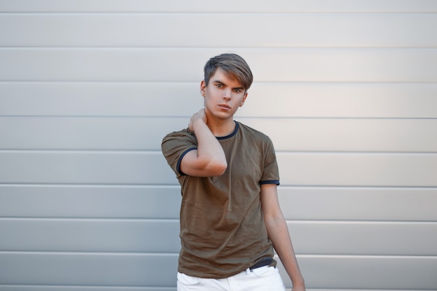 Homem bonito elegante com um penteado em uma camisa verde elegante perto da parede de metal