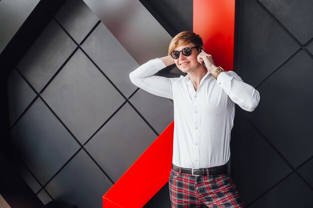 Foto homem bonito elegante em pé perto moderno edifício preto e falando por telefone