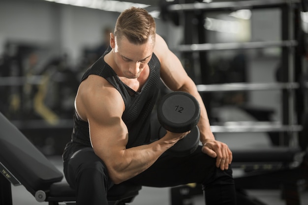 homem bonito em boa forma com músculos na academia fazendo exercícios com halteres