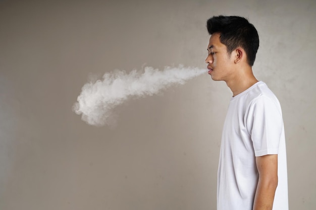 Homem bonito em camiseta branca emite fumaça de vape