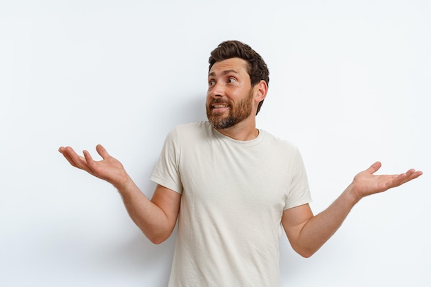 Homem bonito em camiseta elegante em pé sobre fundo branco abriu as mãos e mostra surpresa