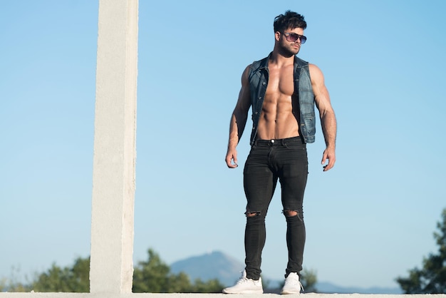 Homem bonito em pé forte e posando ao ar livre usando jeans preto fundo do céu