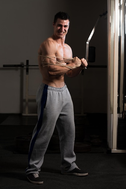 Homem bonito em pé forte na academia e flexionando os músculos com cabo muscular atlético fisiculturista modelo fitness posando após exercícios
