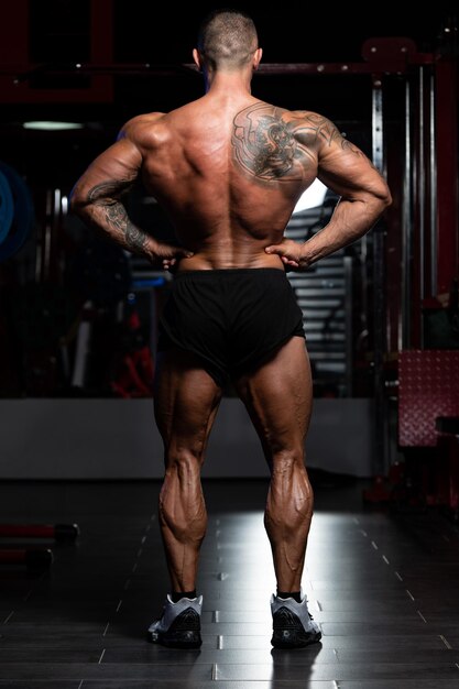 Homem bonito em pé forte na academia e flexionando os músculos Muscular Atlético Fisiculturista Modelo de fitness posando após exercícios