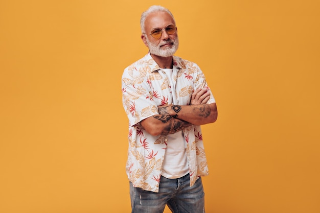 Homem bonito em pose de camisa de praia e óculos de sol na parede laranja