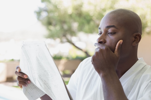 Homem bonito em roupão de leitura de jornal fora