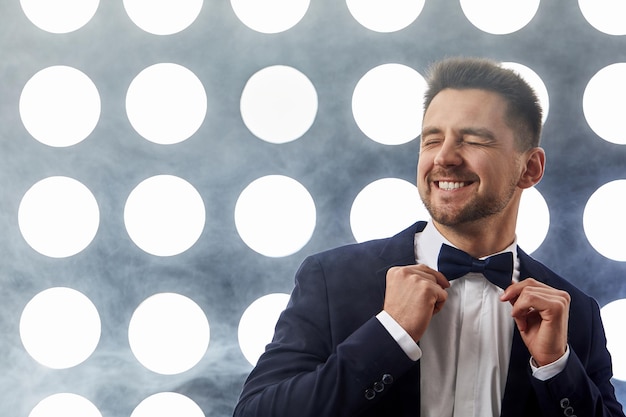 Homem bonito em smoking posando contra o pano de fundo dos holofotes