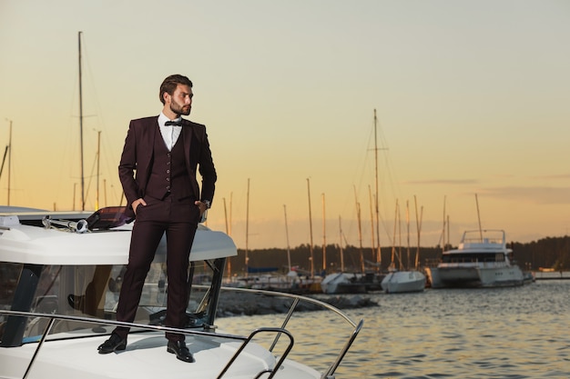 Foto homem bonito em uma regata. jovem em pé no iate no mar ao pôr do sol