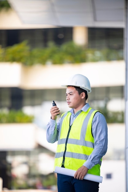 Homem bonito engenheiro asiático ou arquiteto falando ao telefone com engenheiro chefe usa capacete de segurança branco